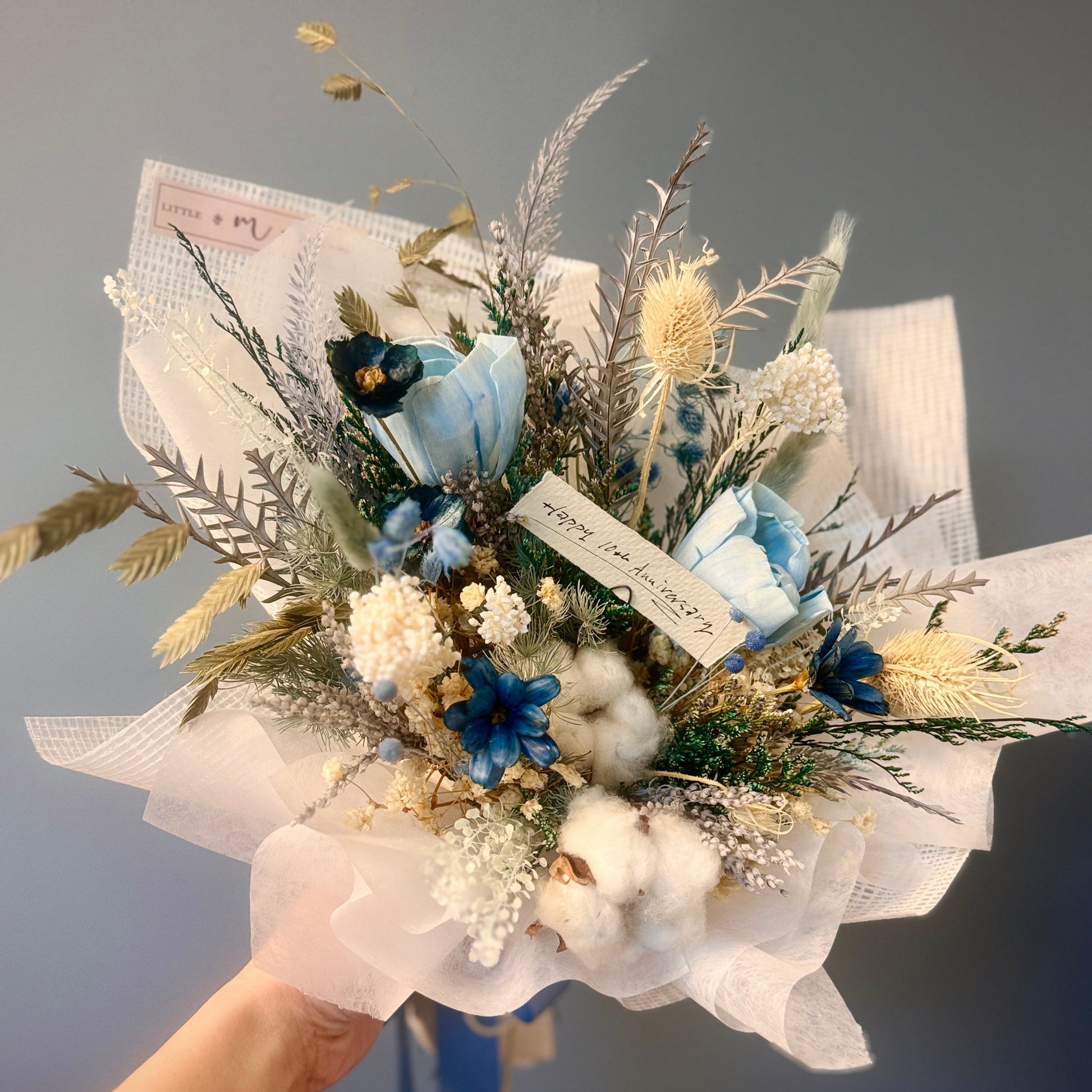 Bouquet of dried flowers with blue and white tones held against a gray background